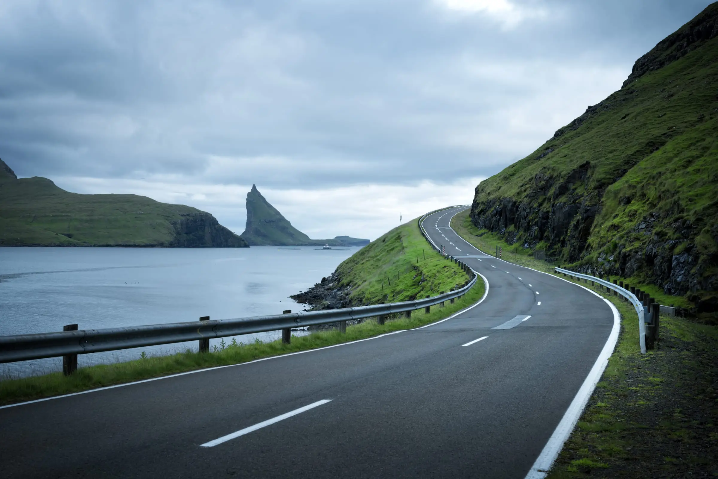 A road winding between green mountains by the sea in the Faroe Islands